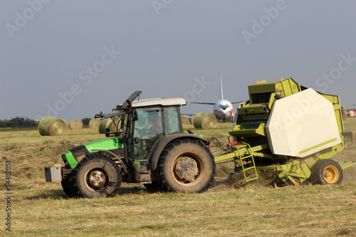 Tractor collecting haystack in the field at the airfield