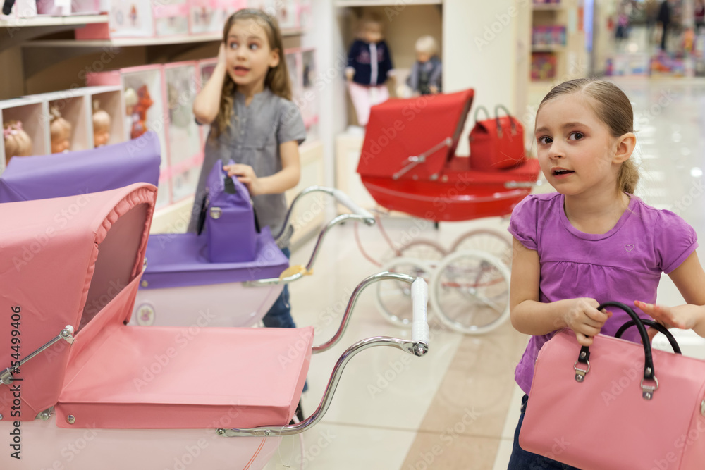 Two girls in toy store with rows of dolls purchased buggy Two girls in toy store with rows of dolls purchased buggy