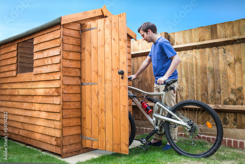 Fototapeta Man pushing his bike into a shed for storage