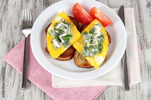 Scrambled eggs and toast on plate on napkin on wooden table