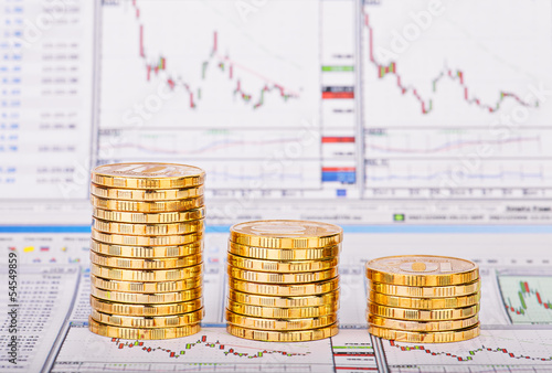 Down trend stacks of golden coins and financial chart as the bac