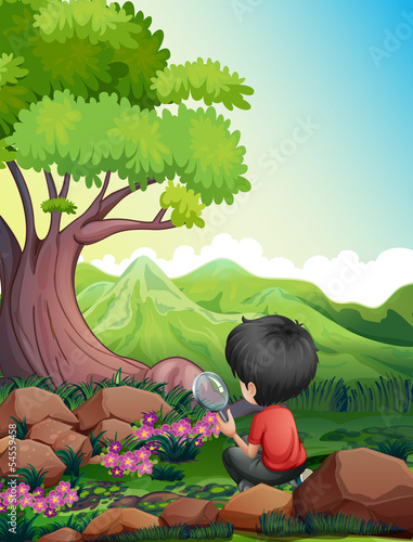 A boy holding a magnifying glass while looking at the flowers