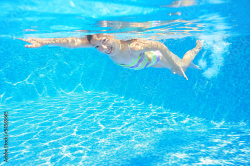 Happy active child swims freestyle in pool, underwater view