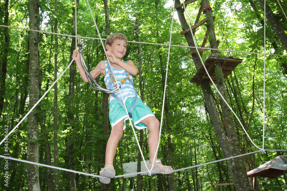 young happy child boy in adventure park in safety equipment