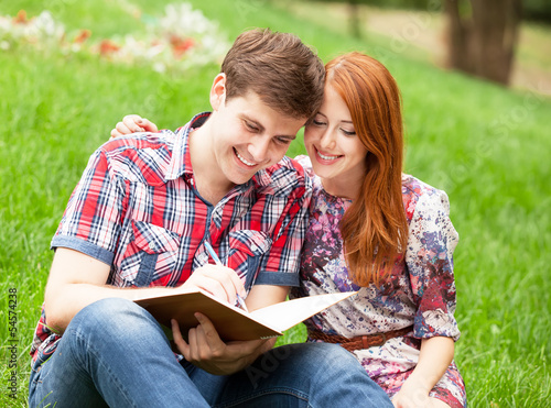 Young students sitting on green grass with note book.