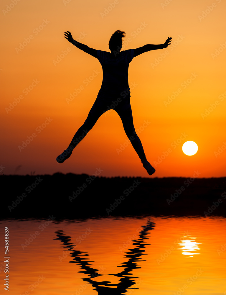 Silhouette woman jumping against orange sunset