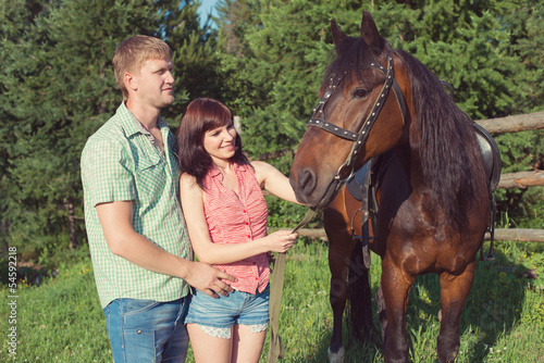 Happy caucasian couple bonding with a brown horse
