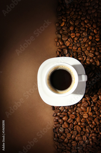 Cup of coffee with coffee beans on brown background