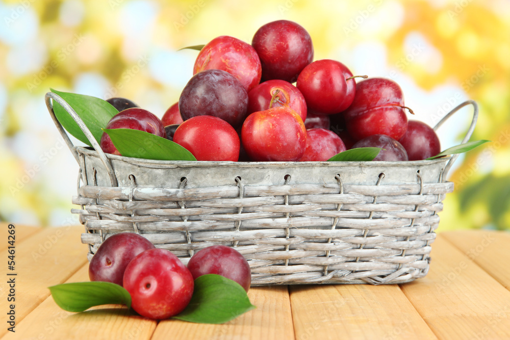 Ripe plums in basket on wooden table on natural background Ripe plums in basket on wooden table on natural background
