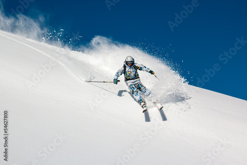 Skier on a steep mountain slope. In turn raises the snow dust.