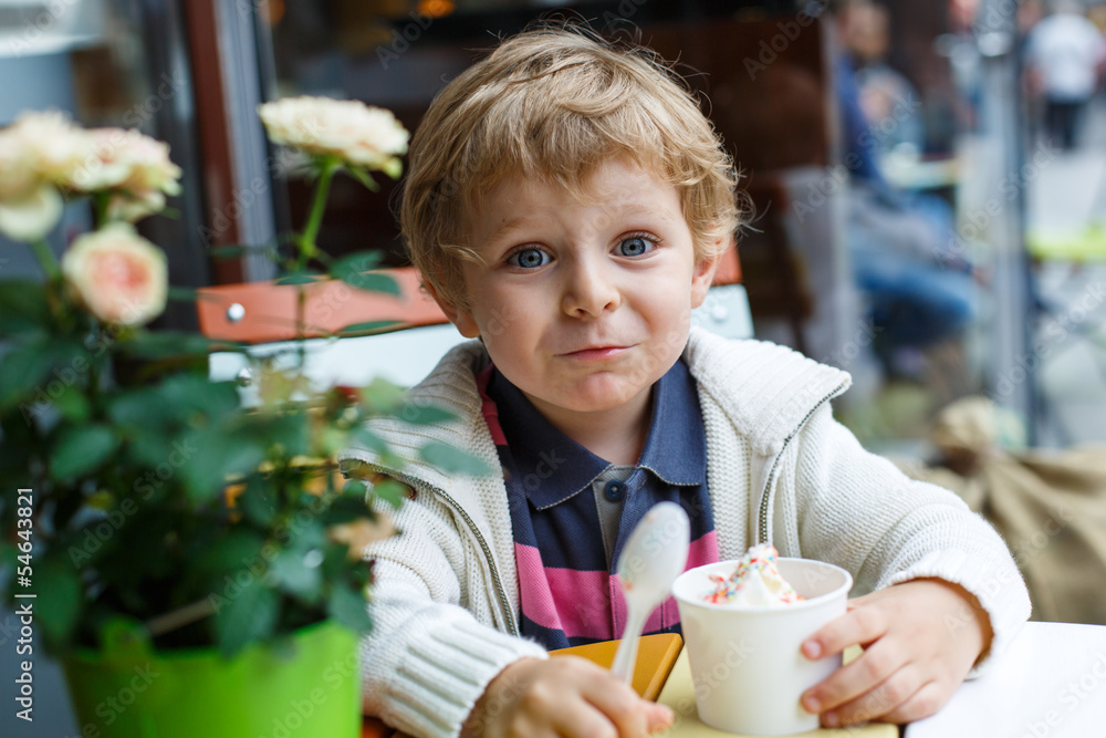 Fototapeta premium Adorable little boy eating frozen yoghurt ice cream in cafe