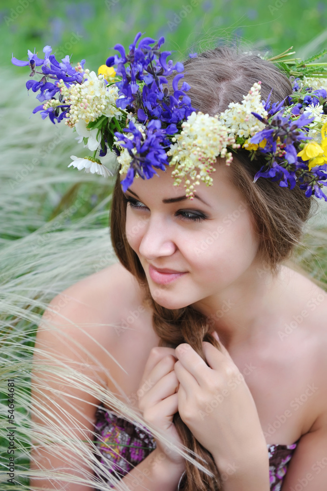 Naklejka premium Beautiful young woman with flower wreath in the grass of feather