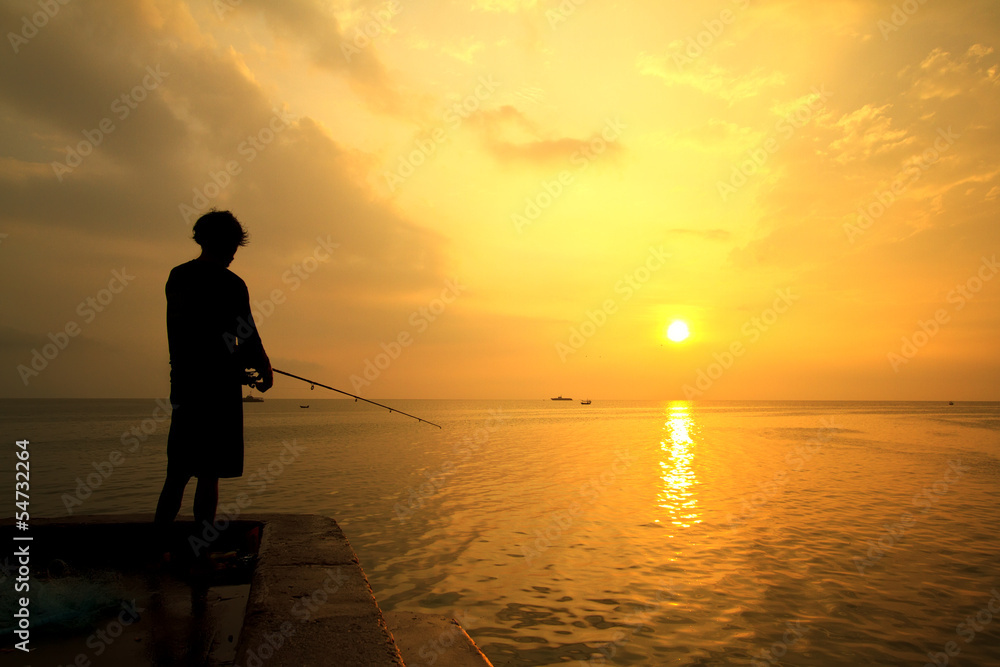 Fisherman fishes on the sea. Silhouette at sunrise