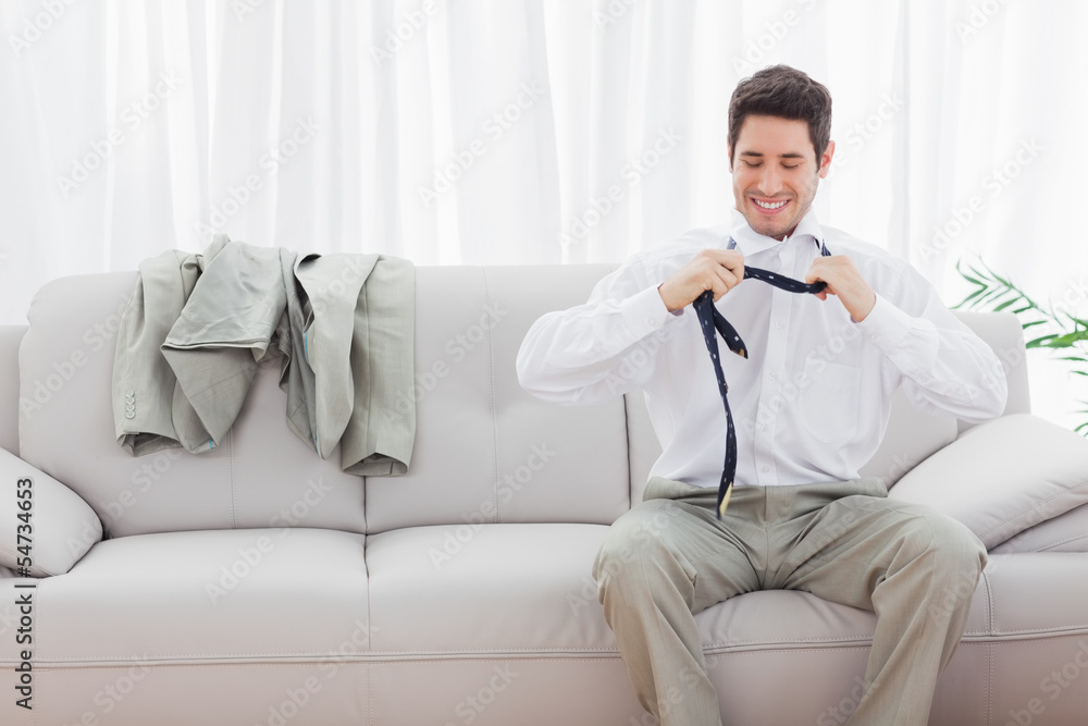 Smiling businessman sitting on sofa loosening his tie Smiling businessman sitting on sofa loosening his tie