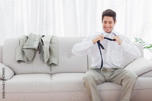 Smiling businessman sitting on sofa loosening his tie