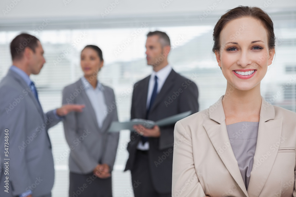 Smiling businesswoman posing while colleagues talking together Smiling businesswoman posing while colleagues talking together