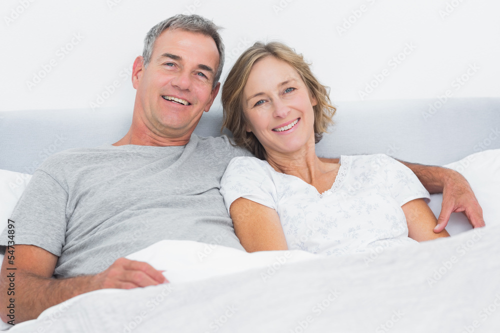 Happy couple cuddling in bed looking at camera Happy couple cuddling in bed looking at camera