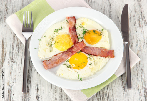 Scrambled eggs and bacon on plate on napkin on wooden table