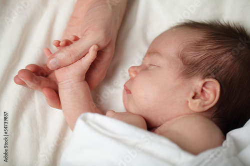 Happy newborn - baby sleeping and holding his father's hand