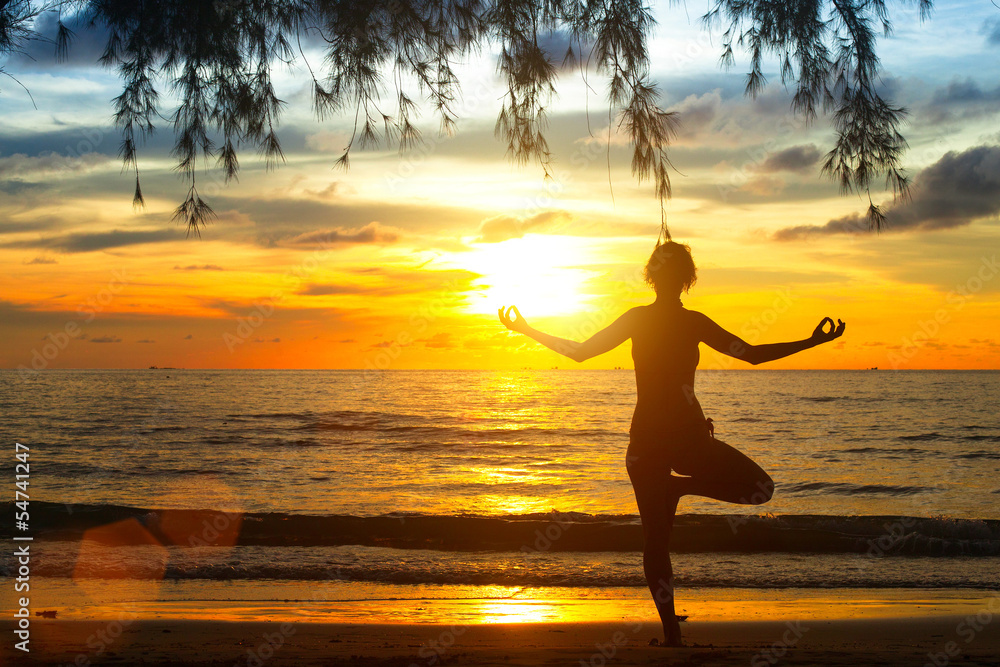 Young woman practicing yoga at sunset on the coast of Thailand