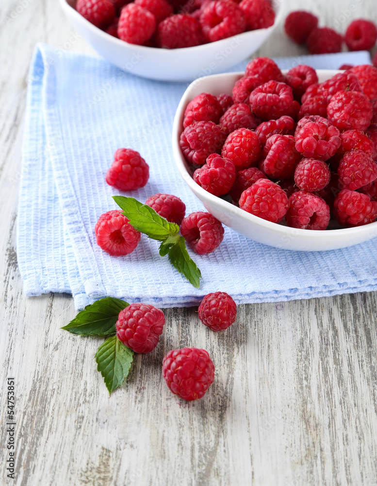 Ripe sweet raspberries in bowls on wooden background