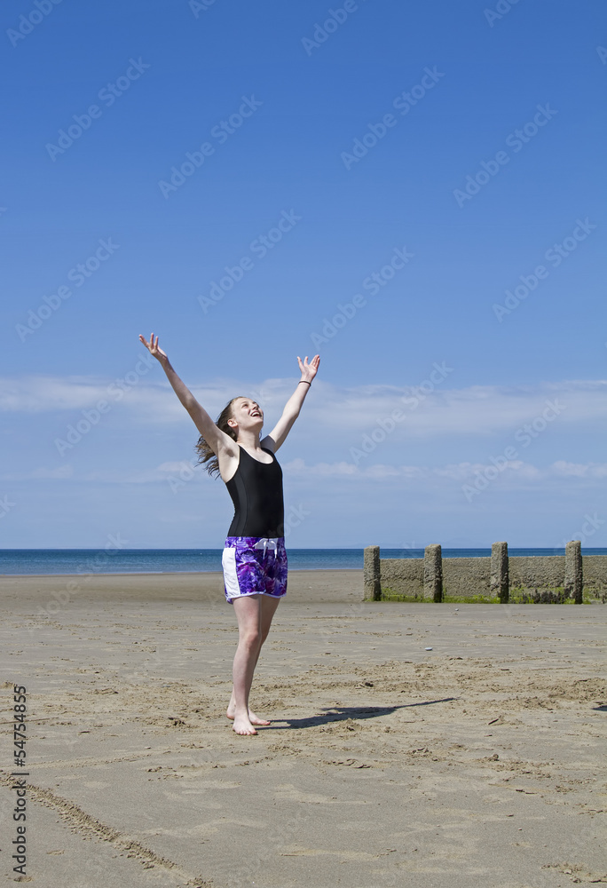 Young girl on beach raising her hands to the sky