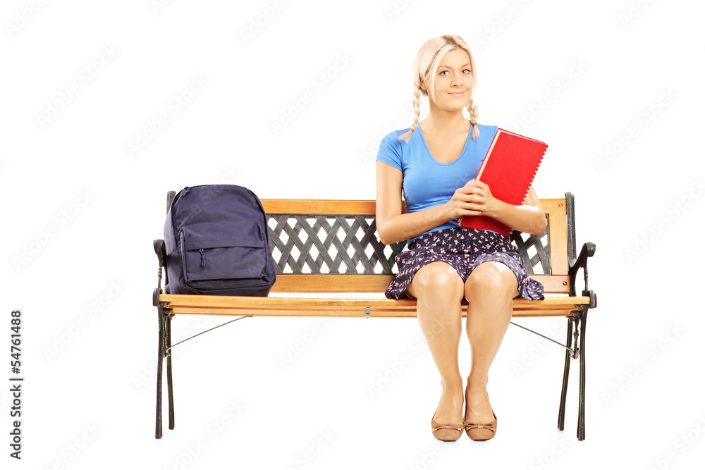 Smiling female student sitting on a wooden bench and holding a n Smiling female student sitting on a wooden bench and holding a n