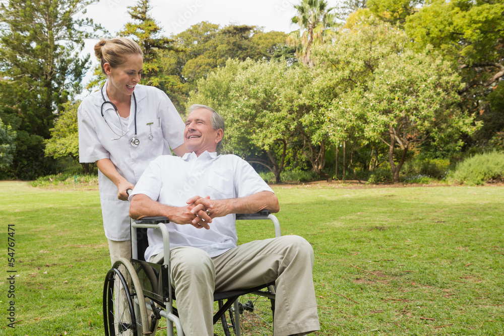 Smiling man sitting in a wheelchair talking with his nurse pushi Smiling man sitting in a wheelchair talking with his nurse pushi
