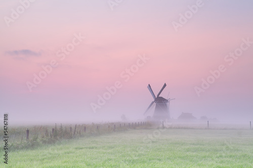 windmill on meadow in morning fog