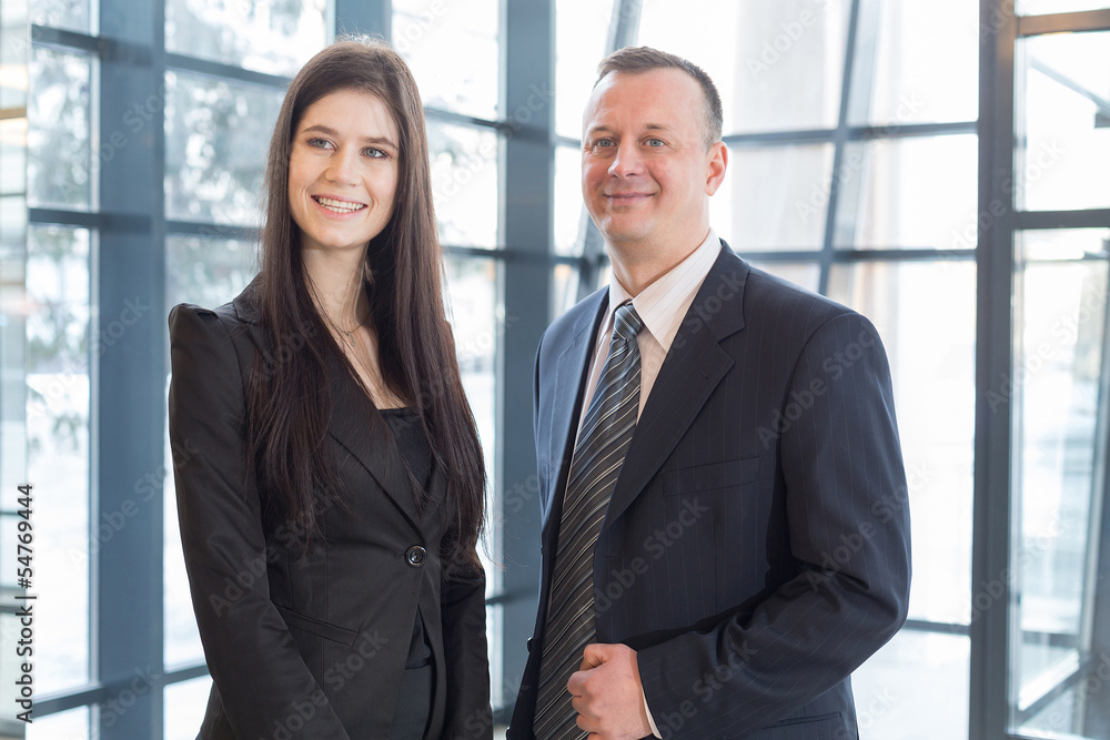 Smiling man and woman in business suits stand near windows