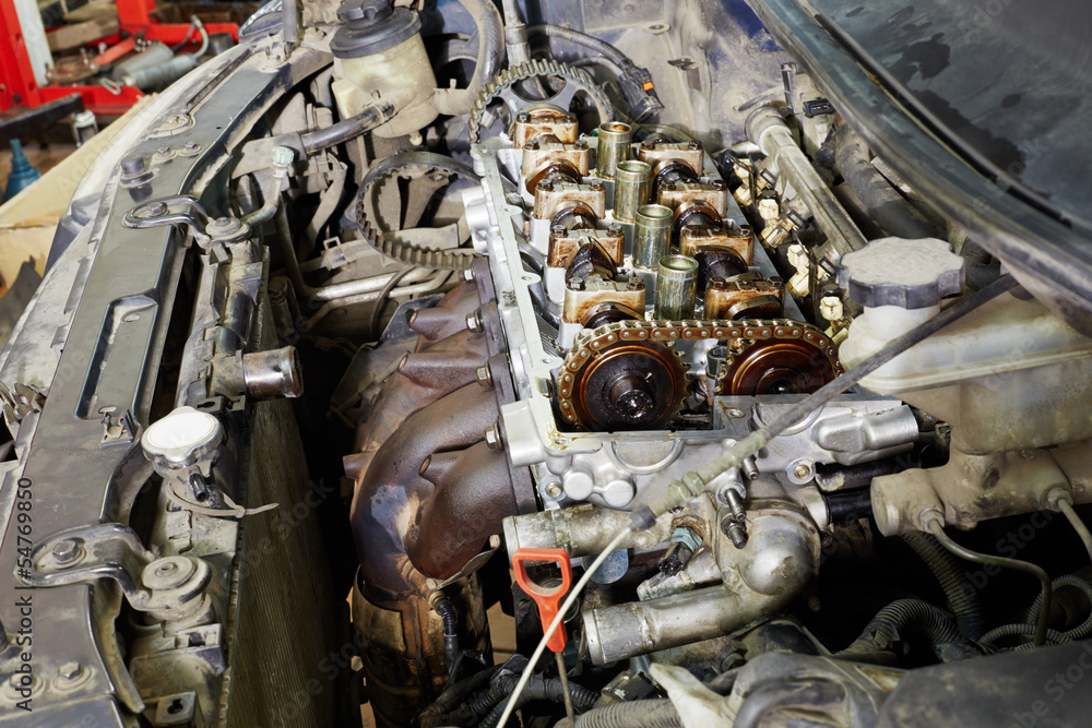 Four-cylinder car engine with cover off under open car hood Four-cylinder car engine with cover off under open car hood