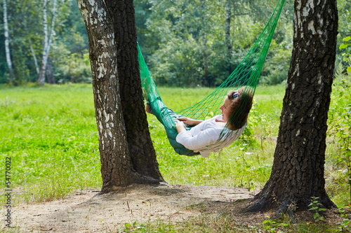 Young woman lies in hammock suspended between two thick birches