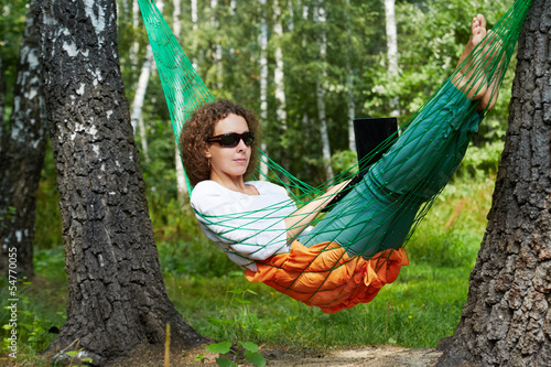 Young woman in dark sunglasses lies in hammock outdoors and work