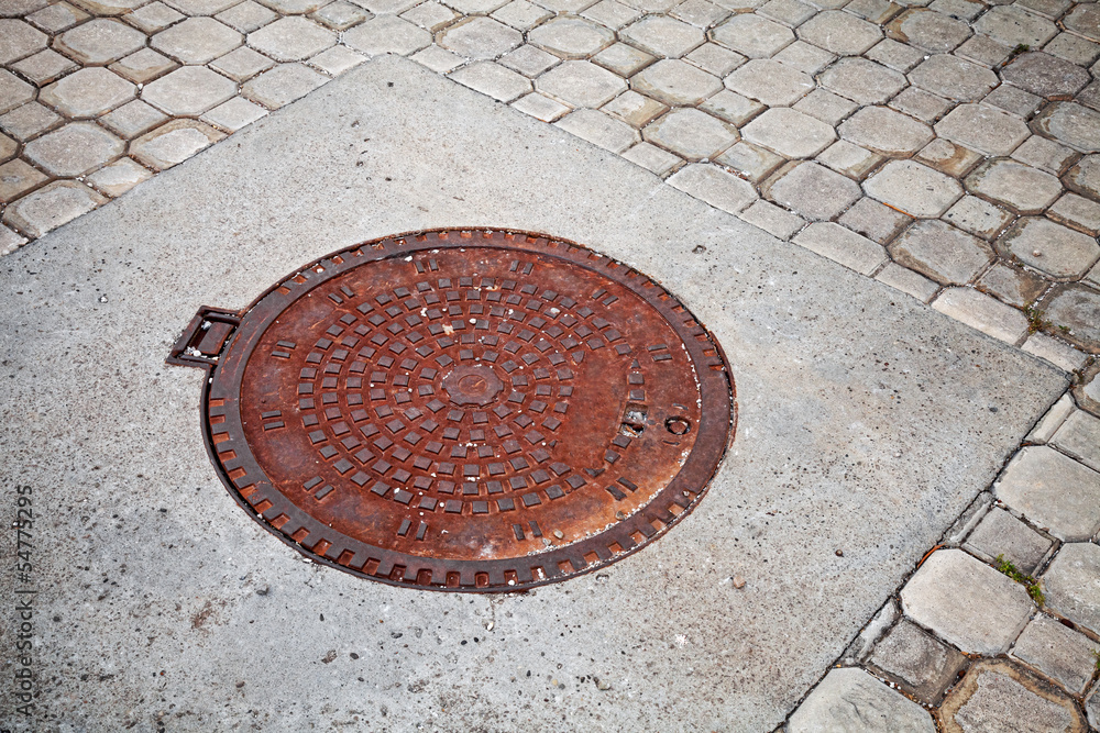 Old rusted sewer manhole on the cobblestone road Old rusted sewer manhole on the cobblestone road