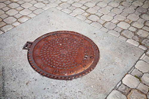 Old rusted sewer manhole on the cobblestone road