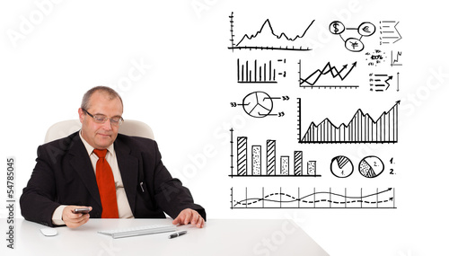 Businessman sitting at desk with diagrams and holding a mobileph