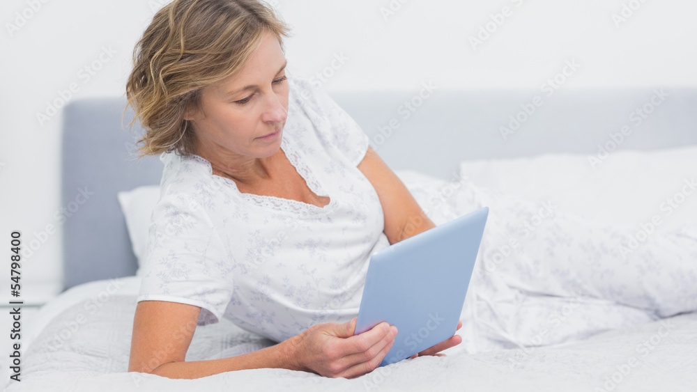 Happy blonde woman lying on bed using tablet pc