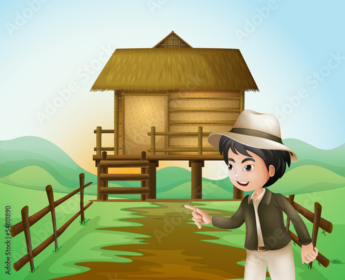 A boy with a hat standing near the nipa hut