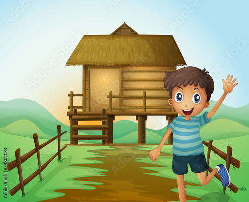 A boy waving his hand in front of a nipa hut
