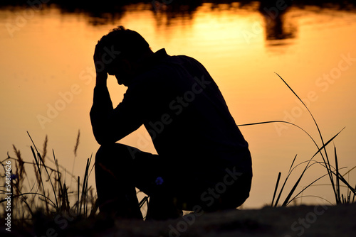 depressed man sitting against the light reflected in the water photo