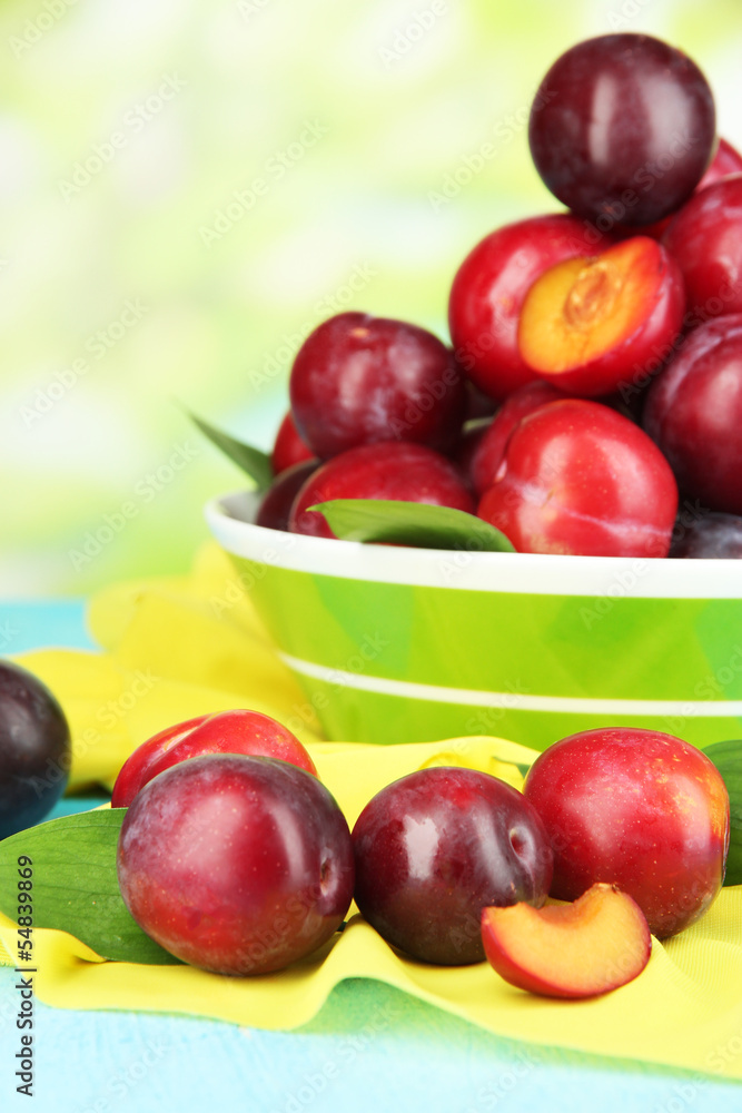 Ripe plums in bowl on wooden table on natural background Ripe plums in bowl on wooden table on natural background