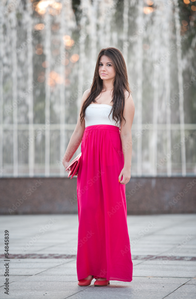 young woman with long red skirt in front of a fountain