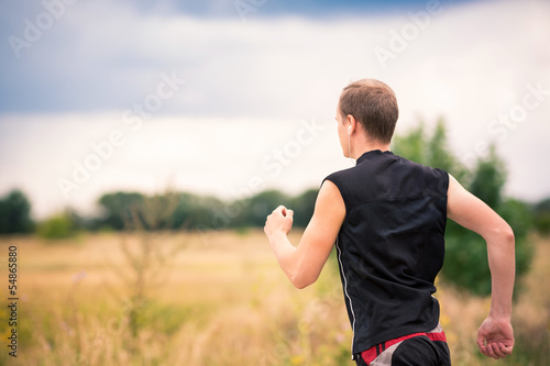 Back of sportive young man jogging outdoor