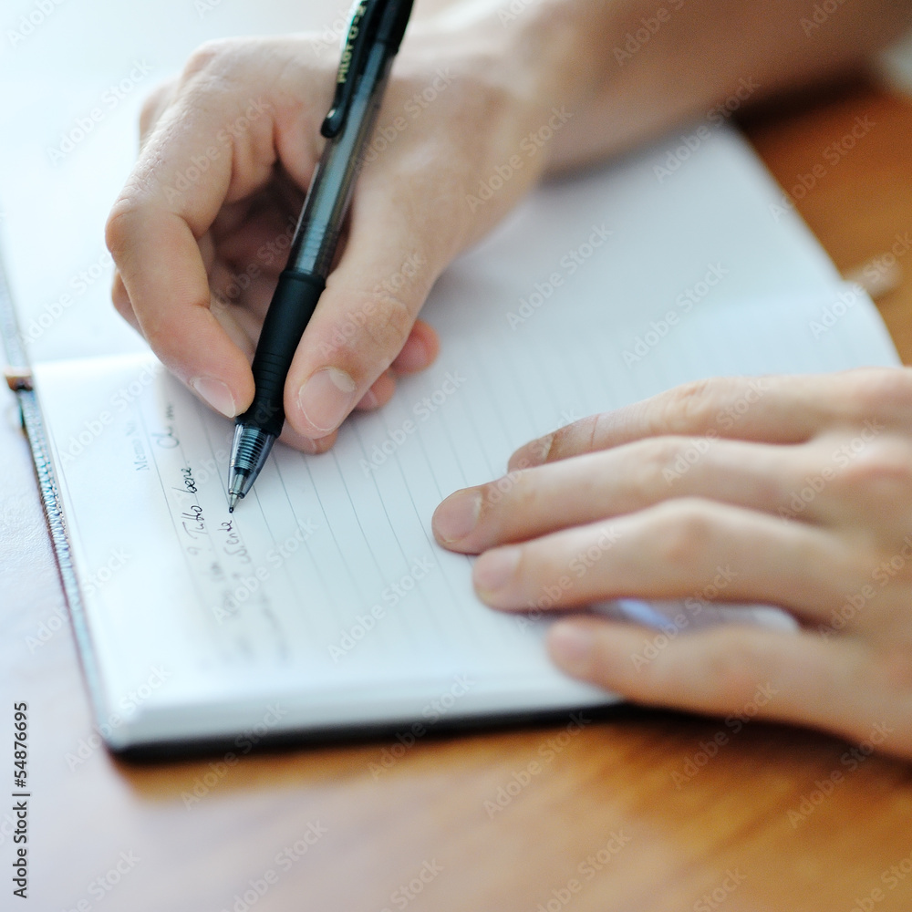 student hand with a pen writing on notebook