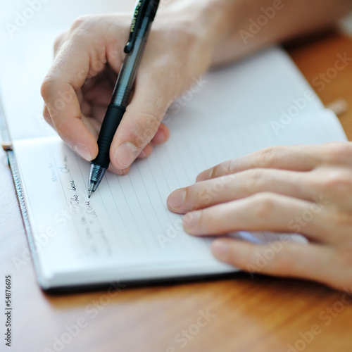 student hand with a pen writing on notebook