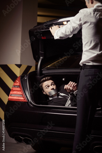 Kidnapped businessman. Tied up young man lying in the car trunk photo