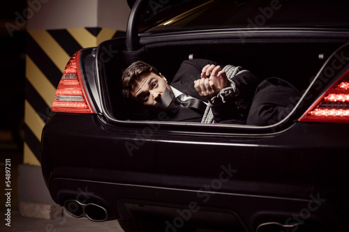 Kidnapped businessman. Tied up businessman lying in the car trun photo