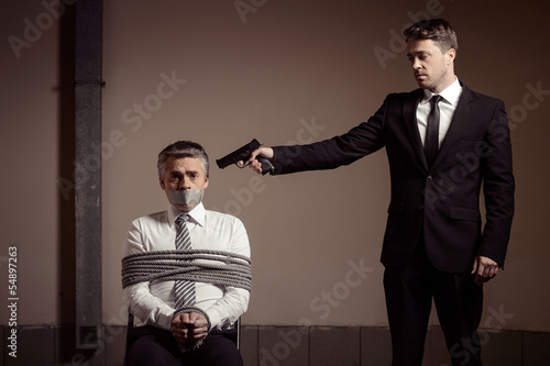 Kidnapper and victim. Tied up businessman sitting at the chair a