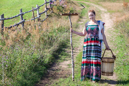 Girl with wooden rake and bucket on country road Copyspace