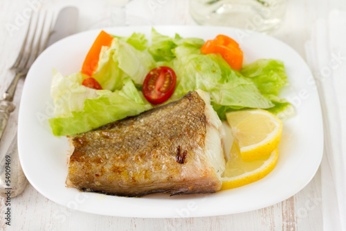fried fish with salad and lemon on white plate